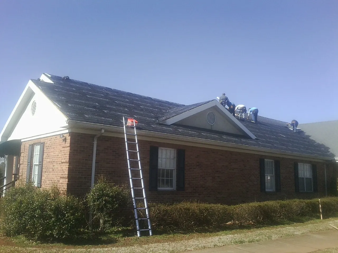 Crew tearing shingles off a brick ranch roof with a ladder set — Emergency Roof Repair work by our crew in Oneco