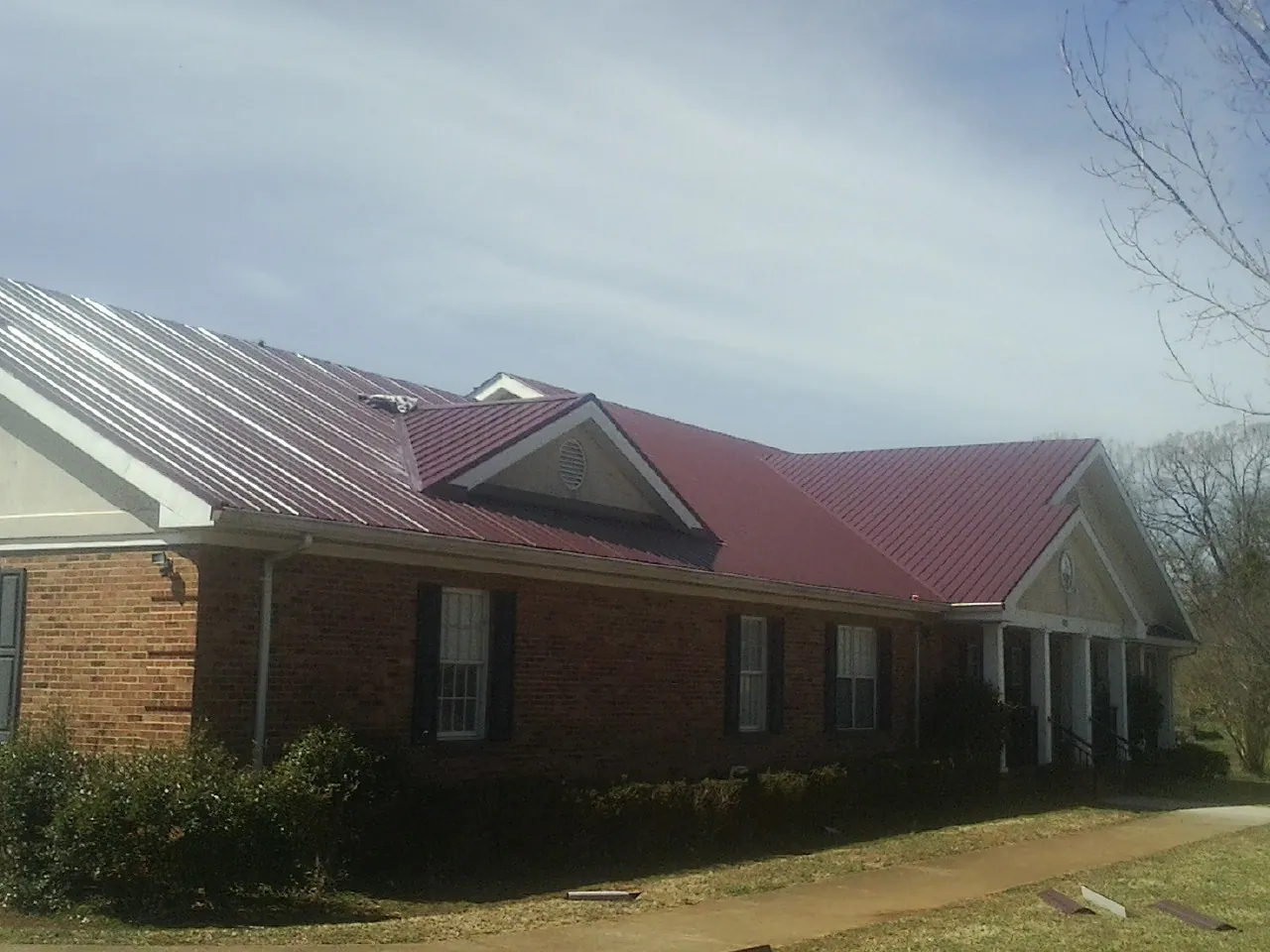Red metal roof with gabled entries on a long brick building, from a Hail Damage Roof Repair job in Oneco