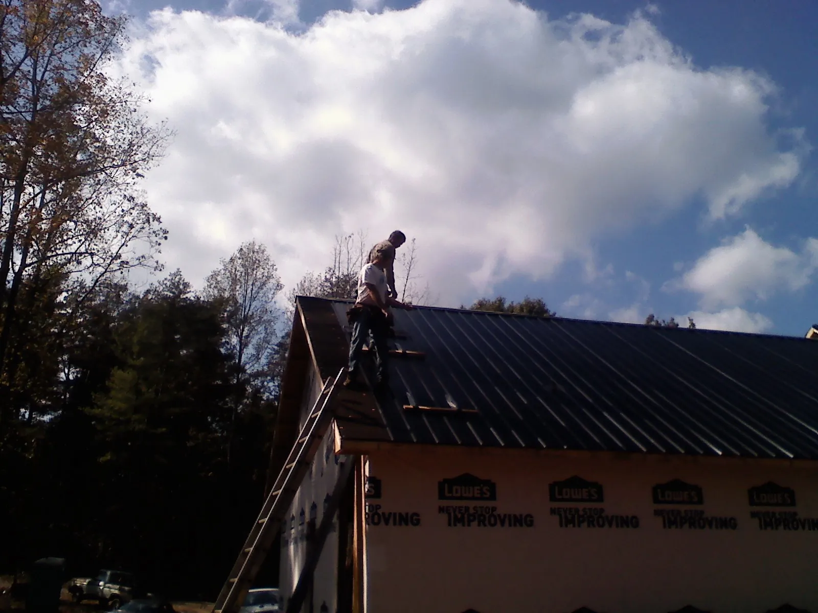 Roofer fastening dark metal panels high against a cloudy sky, from a Roof Inspection job in Oneco