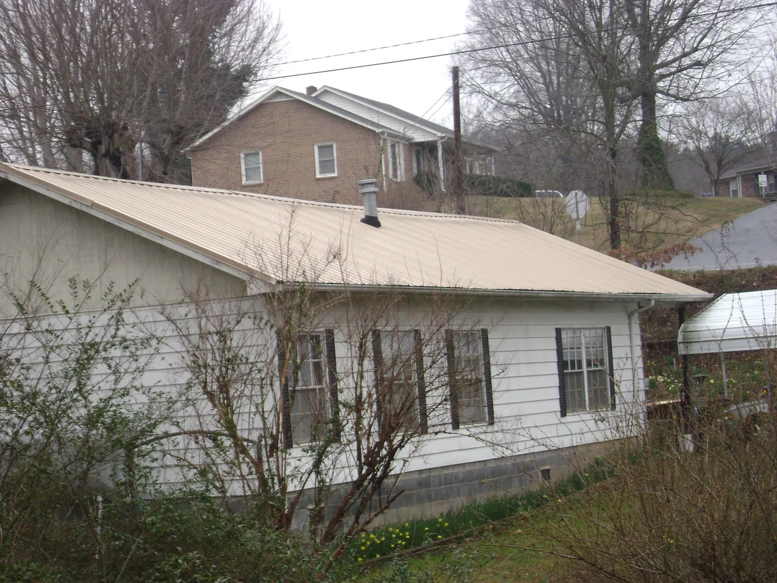 Tan metal roof on a white sided house set into a hillside — Commercial Roofing by Roofing Brothers in Oneco